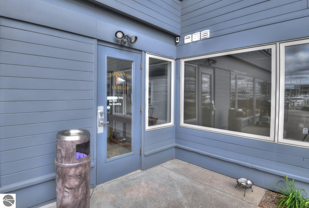 Entrance of Harbor West Yacht Club featuring blue siding, large windows, and a sign indicating "No Pets, No Smoking," with a waste bin nearby, located in Traverse City, Michigan.