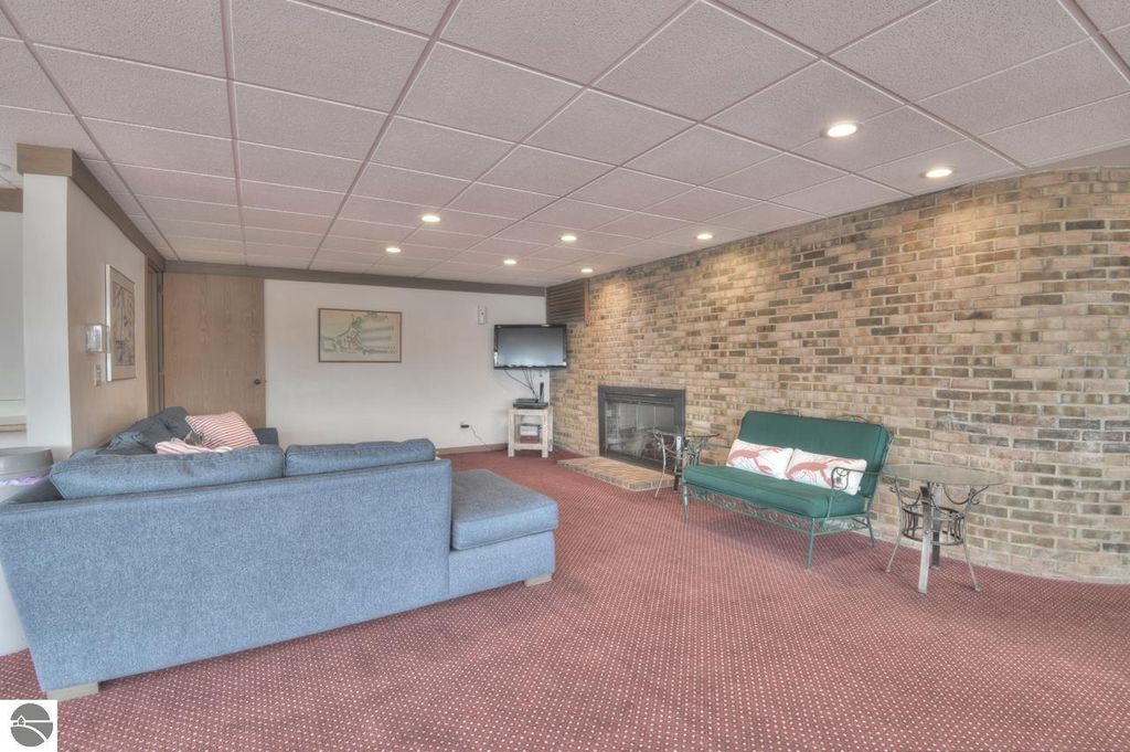 Living area with gray sofa, green loveseat, brick wall, and fireplace, showcasing cozy interior design for Traverse City property listing.