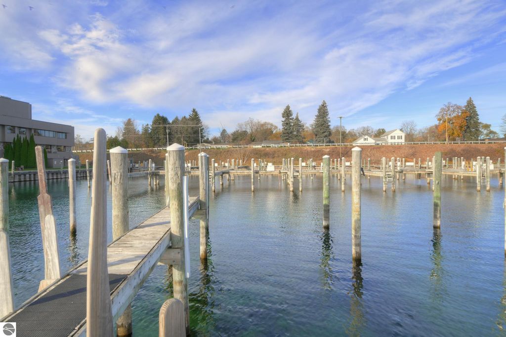 Marina with wooden docks and slips on clear water, surrounded by trees and residential buildings, located in Traverse City, Michigan, highlighting boating opportunities and waterfront access.