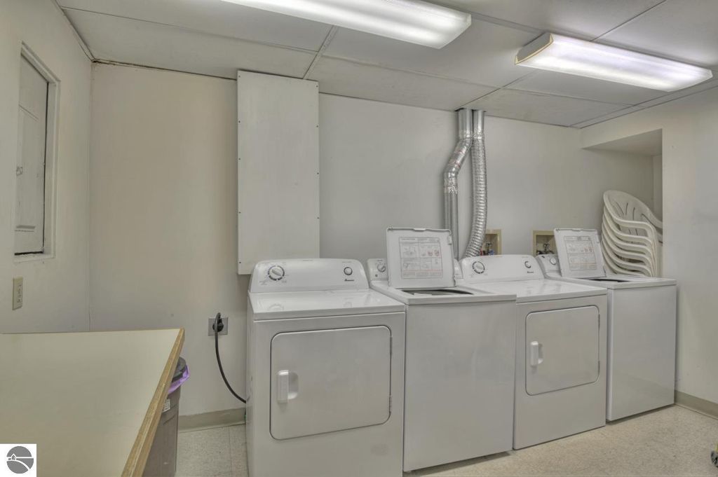 Laundry room featuring three white washing machines, dryer, and storage shelves in a clean, well-lit space.