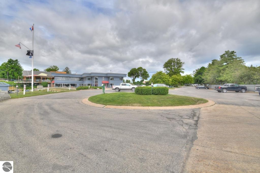 Exterior view of a marina facility in Traverse City, Michigan, featuring parking area, landscaped greenery, and flags, highlighting the location's access to West Bay and nearby amenities.