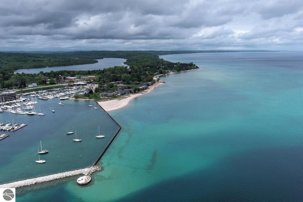 Aerial view of the private marina at Traverse City, showcasing sailboats docked in the harbor, turquoise waters of West Bay, and surrounding lush greenery, highlighting the scenic location near 12755 S Marina Village Drive.