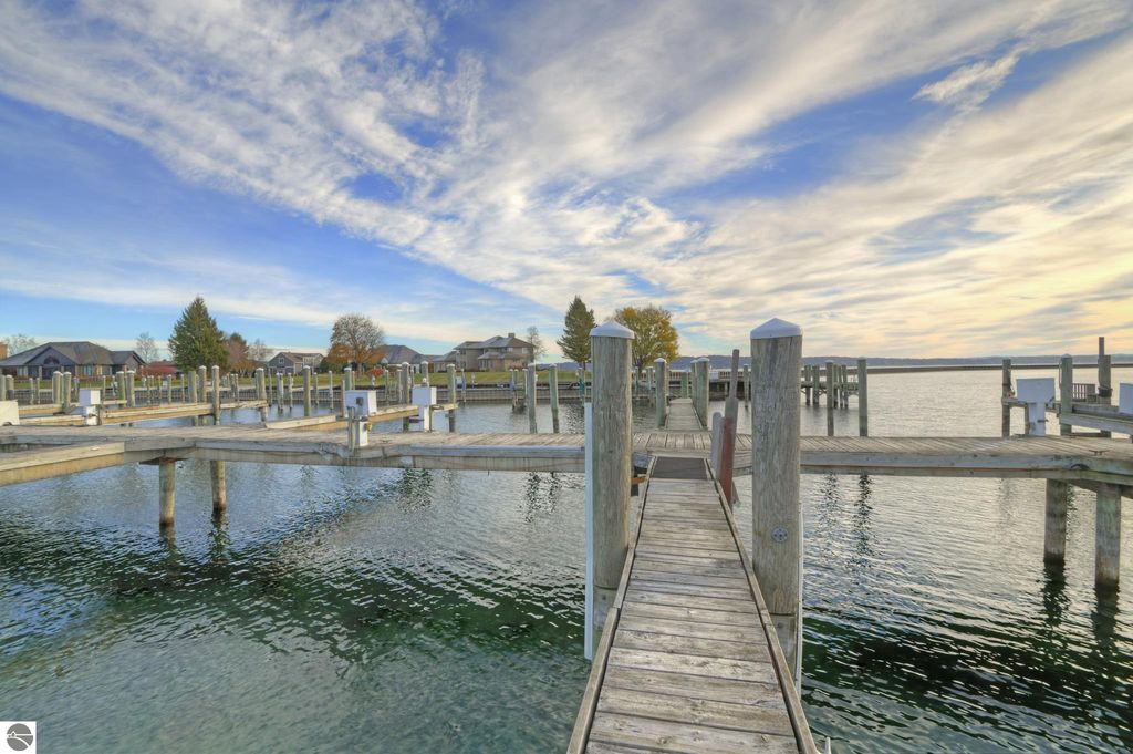 Wooden dock extending into calm waters at a marina in Traverse City, surrounded by residential properties and a clear blue sky, emphasizing the boating and waterfront lifestyle.