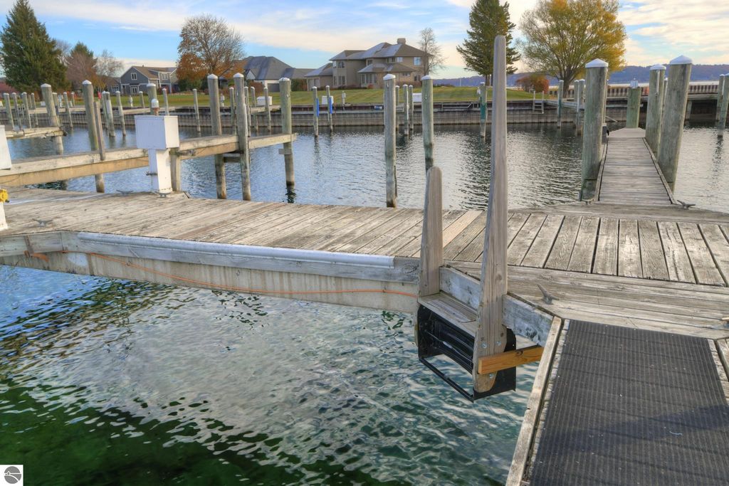 Dock with wooden planks and boat slip at private marina in Traverse City, Michigan, featuring calm water, surrounding trees, and residential buildings in the background.