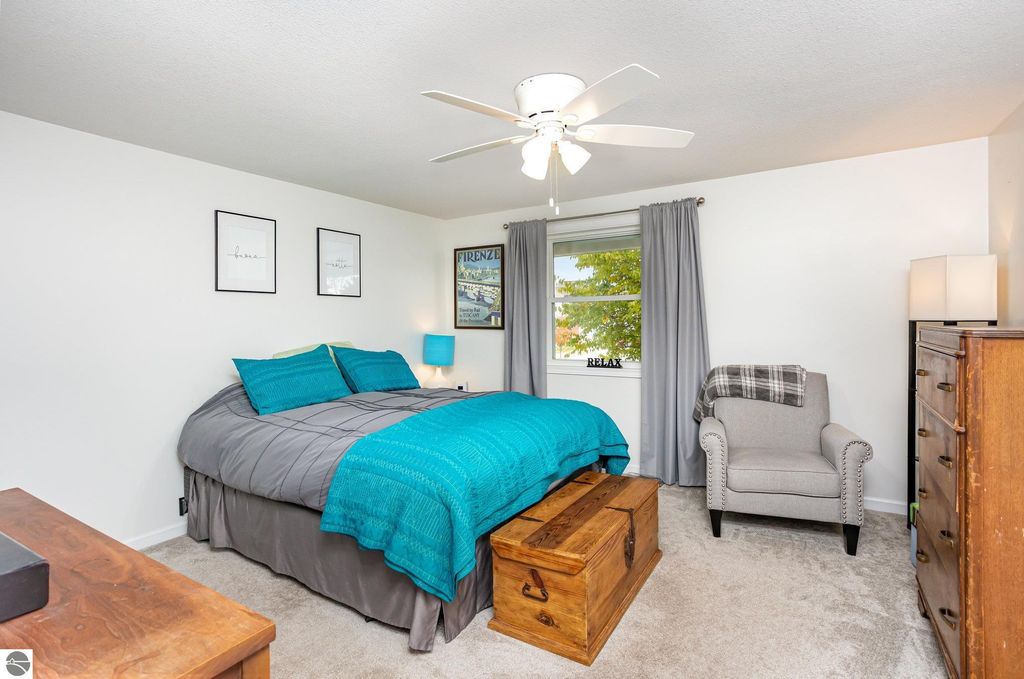 Brightly decorated bedroom featuring a queen-sized bed with turquoise bedding, a cozy armchair, a wooden trunk, and framed wall art, highlighting modern updates in the home at 1932 Churchill Boulevard, Mt Pleasant, MI.