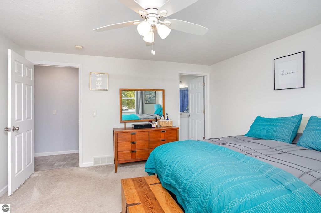 Updated bedroom with turquoise bedding, wooden dresser, modern decor, and natural light from windows, showcasing a fresh and inviting atmosphere.