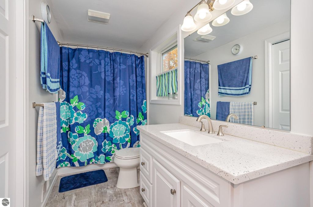 Updated bathroom featuring a modern vanity with a white countertop, blue floral shower curtain, and vibrant towels, reflecting the home's recent renovations at 1932 Churchill Boulevard, Mt Pleasant, MI.