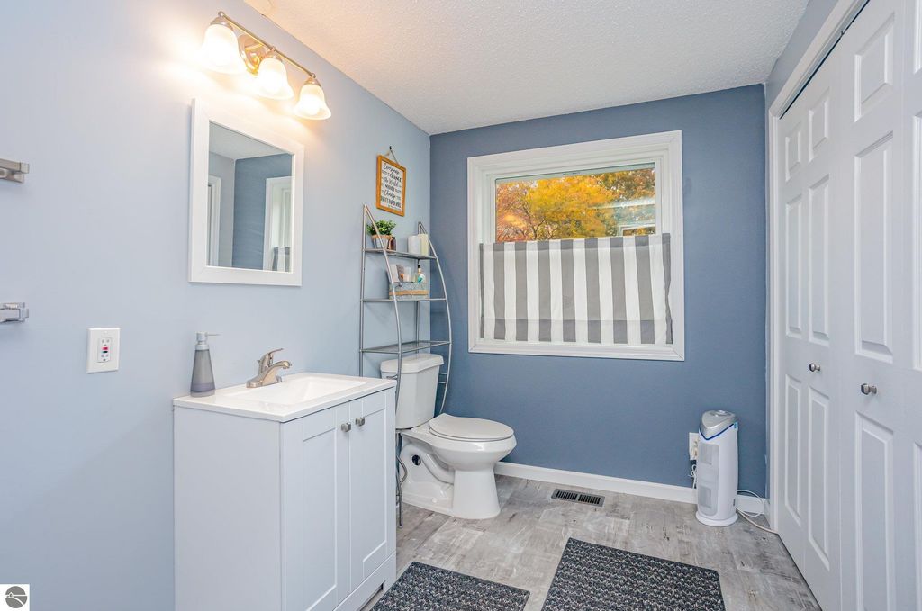 Updated bathroom with modern fixtures, gray walls, white vanity, mirror, and striped window treatment, showcasing a bright and inviting space.