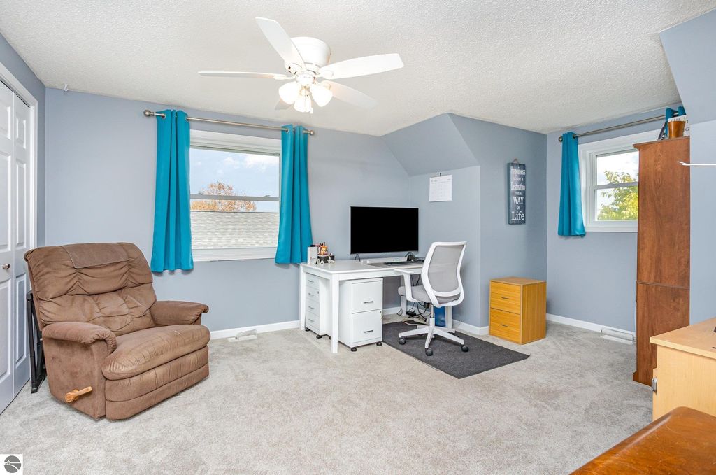 Updated home office featuring a comfortable recliner, modern desk with computer, and bright blue curtains, showcasing natural light and inviting atmosphere in a 3-bedroom property at 1932 Churchill Boulevard, Mt Pleasant, MI.