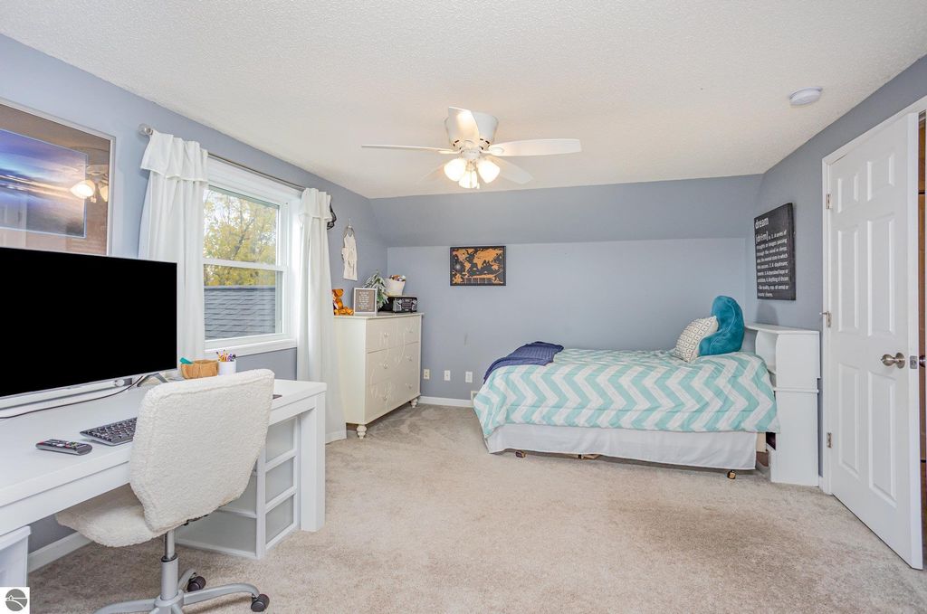 Updated bedroom featuring a bed with a chevron-patterned blanket, a desk with a computer, and large windows allowing natural light, showcasing modern decor and a cozy atmosphere in a home for sale at 1932 Churchill Boulevard, Mt Pleasant, MI.