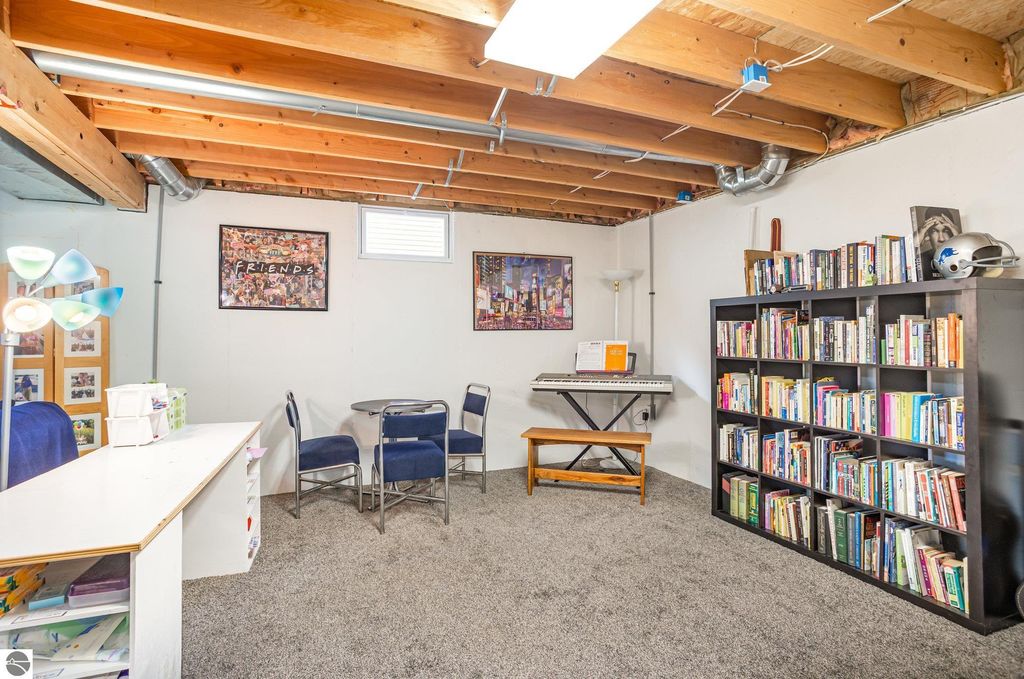 Basement room featuring a cozy carpeted space with a piano, bookshelves filled with books, and framed artwork, ideal for a home office or leisure area in the updated 3-bedroom property at 1932 Churchill Boulevard, Mt Pleasant, MI.