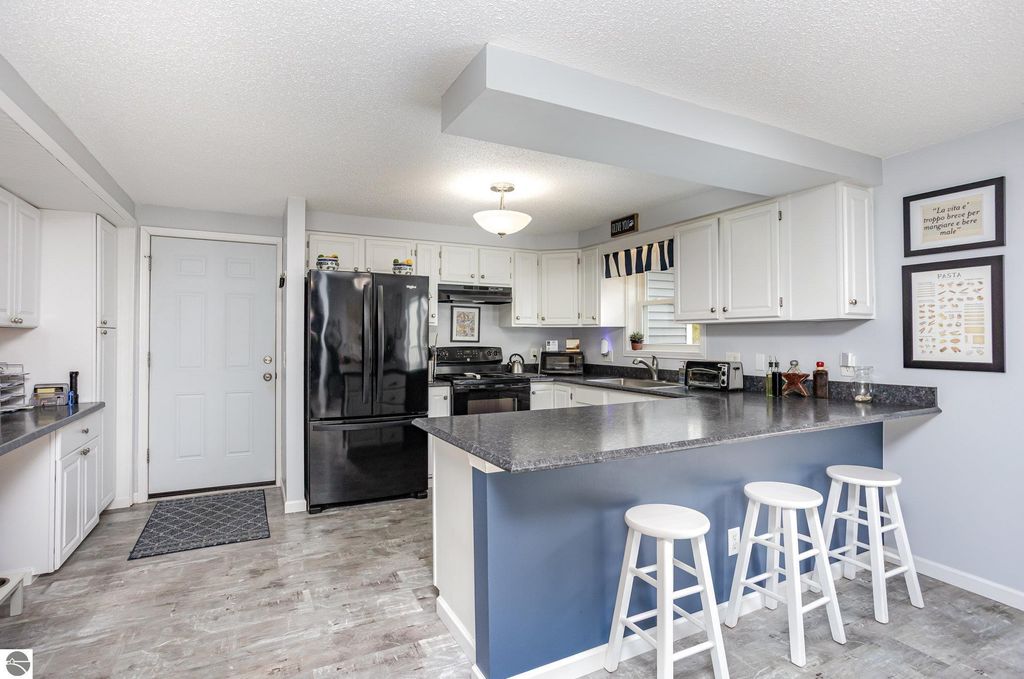 Modern kitchen with white cabinets, black appliances, and a breakfast bar featuring three white stools, showcasing an inviting space in a 3-bedroom home for sale at 1932 Churchill Boulevard, Mt Pleasant, MI.