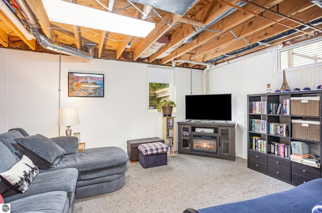 Cozy basement living area featuring a sectional sofa, television, and bookshelf, with natural light from a window and modern decor elements.