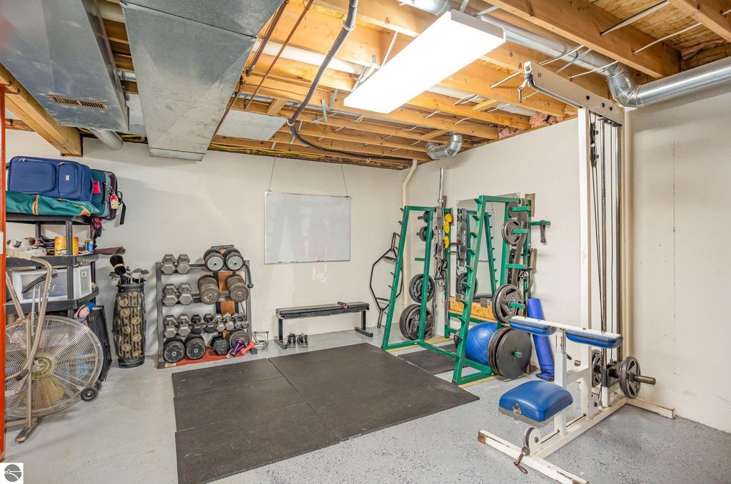 Home gym in basement featuring weightlifting equipment, dumbbells, exercise bench, and storage for fitness gear, enhancing the potential for a workout space in the property at 1932 Churchill Boulevard, Mt Pleasant, MI.