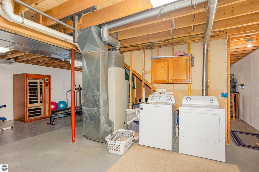 Basement laundry area featuring a washer and dryer, exercise equipment, and a sauna, showcasing potential for additional living space in the home at 1932 Churchill Boulevard, Mt Pleasant, MI.