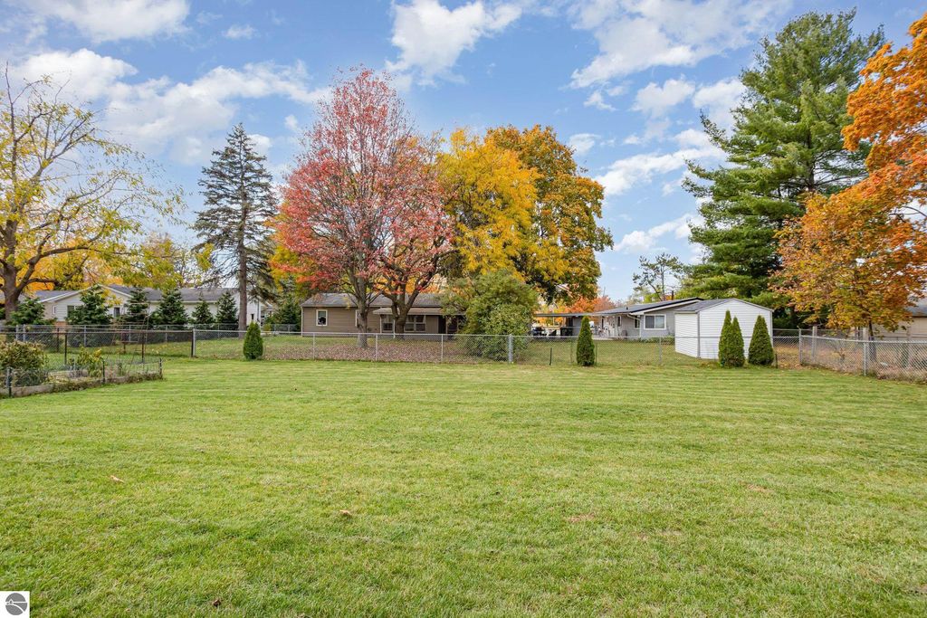 Spacious fenced backyard of a 3-bedroom home at 1932 Churchill Boulevard, featuring vibrant autumn foliage, a well-maintained lawn, and a storage shed, ideal for family activities and outdoor relaxation.