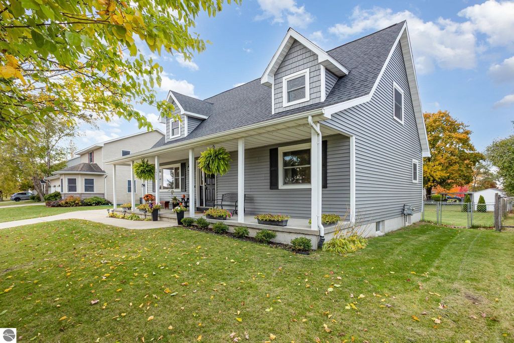 Updated gray home with new roof and siding, featuring a welcoming porch, landscaped front yard, and nearby trees, located at 1932 Churchill Boulevard, Mt Pleasant, MI.