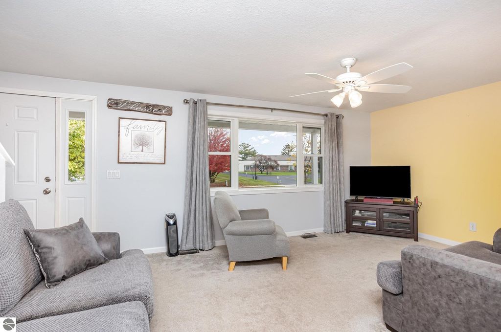 Cozy living room with modern decor, featuring a gray sofa, large window with curtains, and a TV stand, showcasing natural light and inviting atmosphere in a home at 1932 Churchill Boulevard, Mt Pleasant, MI.