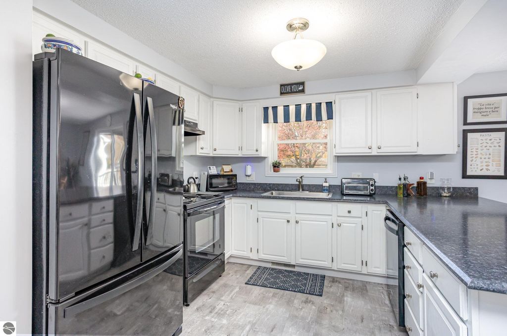 Updated kitchen with black appliances, white cabinetry, and a window showcasing autumn foliage, reflecting modern comfort in a 3-bedroom home for sale at 1932 Churchill Boulevard, Mt Pleasant, MI.