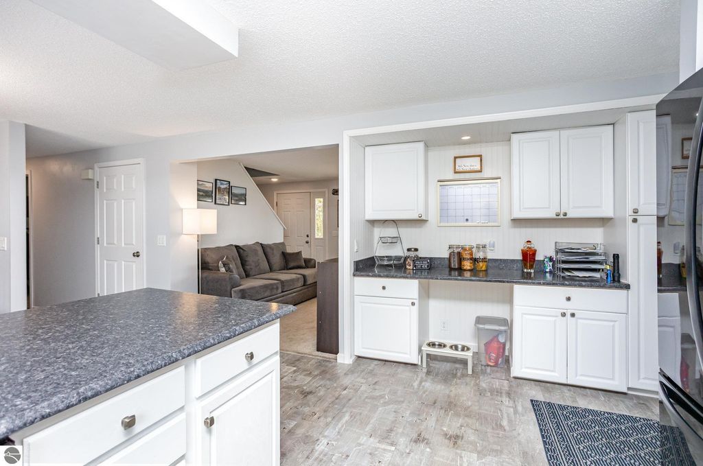 Bright and inviting kitchen with white cabinetry, dark countertops, and a cozy living area visible in the background, showcasing modern updates in the home at 1932 Churchill Boulevard, Mt Pleasant, MI.
