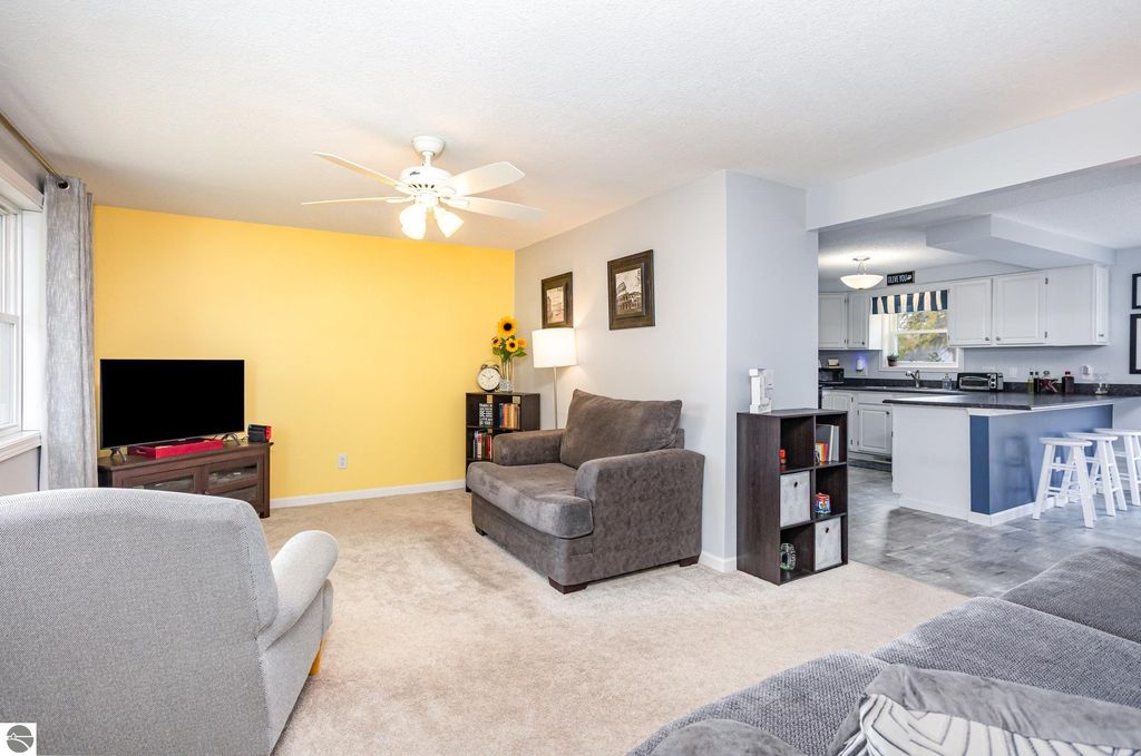 Cozy living room featuring a gray sofa, a light gray armchair, and a yellow accent wall, with a television and modern decor, showcasing the inviting interior of a 3-bedroom home in Mt Pleasant, MI.
