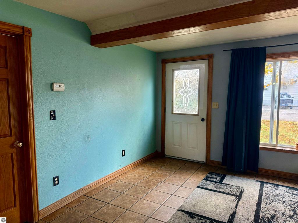 Interior view of a home at 325 Main Street, Breckenridge, MI, featuring a light blue wall, wooden door, tiled floor, and a window with dark curtains, illustrating the spacious living area of the property.