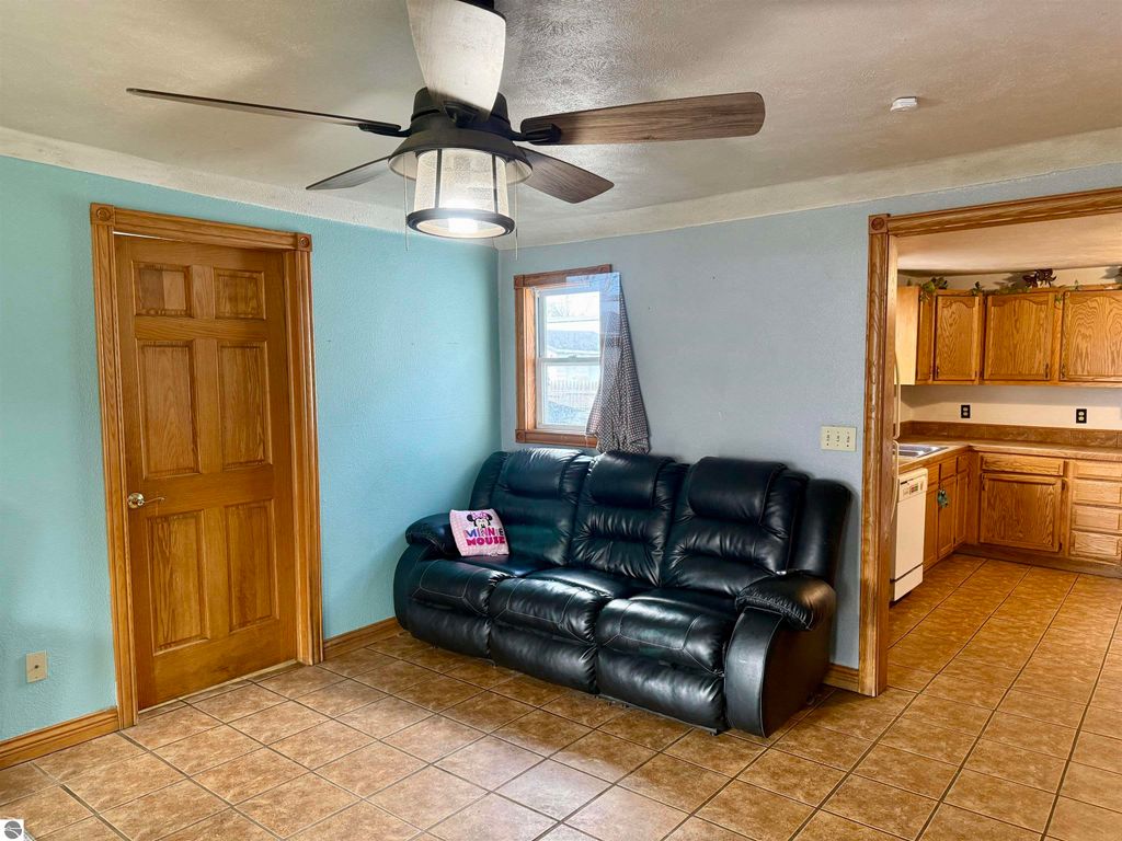 Living room interior of 325 Main Street, Breckenridge, featuring a black leather couch, ceiling fan, and wooden door, with a view into the kitchen area.
