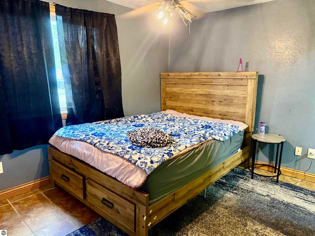 Cozy bedroom featuring a wooden bed frame with storage drawers, blue and white patterned bedding, and black curtains, highlighting the comfortable interior of the home at 325 Main Street, Breckenridge, MI.