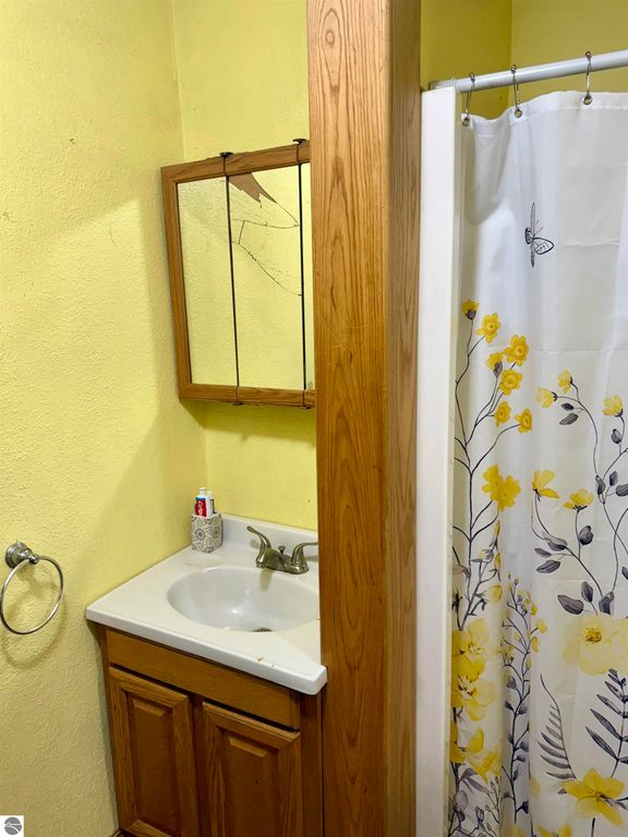 Bathroom with yellow walls, wooden cabinet, sink, and floral shower curtain, reflecting the home's charming and affordable features in Breckenridge, MI.
