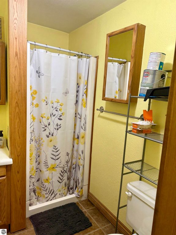 Bathroom featuring a shower with floral curtain, mirror, storage shelf, and toilet, showcasing a cozy and functional space in a Breckenridge home listing.
