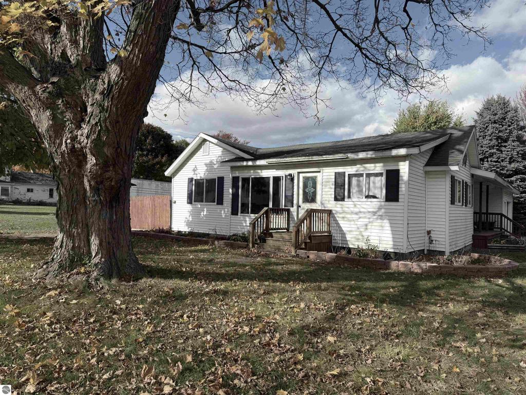 Charming single-family home at 325 Main Street, Breckenridge, MI, featuring a spacious front porch, large windows, and a lush yard with a mature tree, ideal for first-time home buyers.