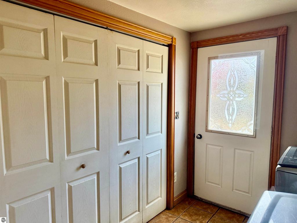 Interior view of a laundry room featuring white double doors, a decorative glass door leading outside, and tiled flooring, highlighting the functional space in the home at 325 Main Street, Breckenridge, MI.