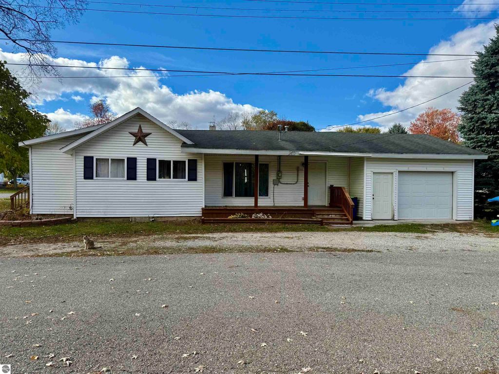 Single-story home at 325 Main Street, Breckenridge, MI, featuring a star decoration on the facade, blue shutters, and a welcoming front porch, surrounded by trees and a gravel driveway.