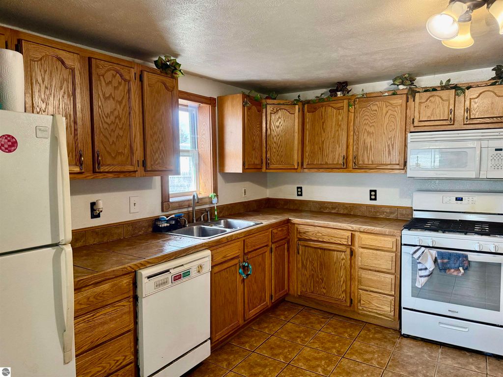 Kitchen interior featuring wooden cabinets, stainless steel appliances, and a tiled countertop, showcasing the spacious layout of the home at 325 Main Street, Breckenridge, MI.