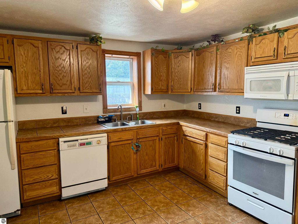 Kitchen interior featuring oak cabinetry, stainless steel appliances, double sink, and tile flooring, showcasing a functional layout ideal for a family home in Breckenridge, MI.