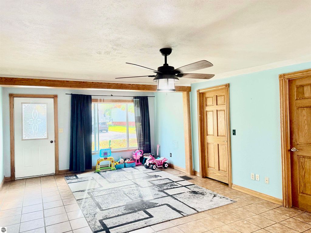 Spacious living room with a ceiling fan, large window, and tile flooring, showcasing children's toys and a cozy atmosphere in a home for sale at 325 Main Street, Breckenridge, MI.