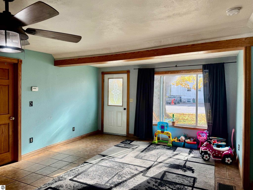 Spacious living room with ceiling fan, large window, and children's toys, showcasing the inviting interior of a 3-bedroom home for sale at 325 Main Street, Breckenridge, MI.