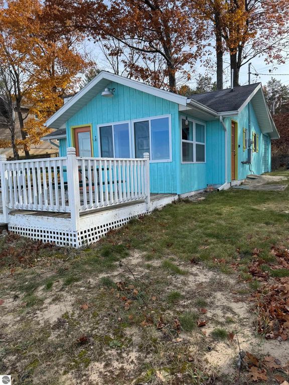 Cottage exterior in Lake City, MI, featuring blue siding, a white porch railing, and surrounded by autumn foliage, showcasing a charming lakeside property for sale on Lake Missaukee.