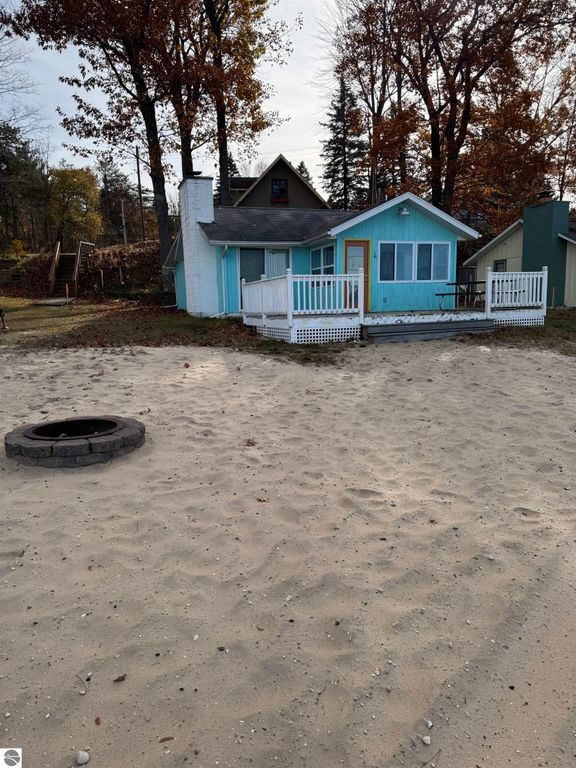 Cottage on Lake Missaukee with turquoise exterior, white porch railing, sandy beach, and fire pit, showcasing charming lakeside living.