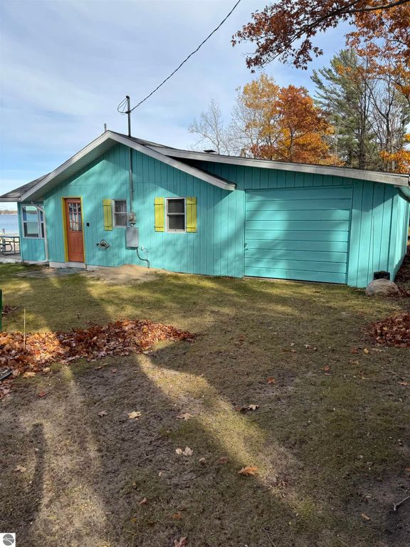 Cottage exterior at 1779 S Green Road, Lake City, MI, featuring teal siding, yellow shutters, and a garage, surrounded by autumn foliage near Lake Missaukee.
