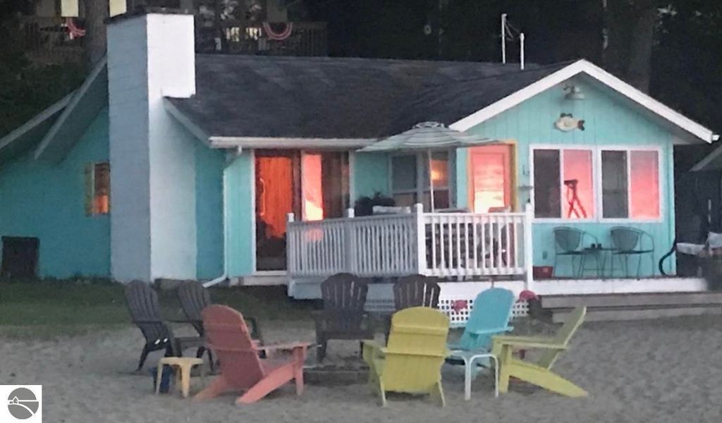 Cottage on Lake Missaukee with colorful Adirondack chairs, featuring a light blue exterior and a porch, perfect for a charming lakeside retreat.
