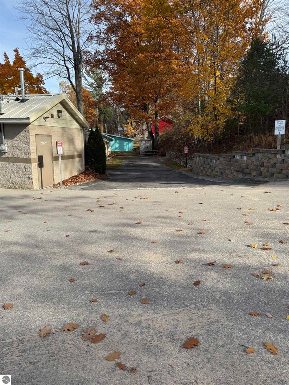 Pathway leading to a charming cottage on Lake Missaukee, surrounded by autumn foliage, with a glimpse of the lake and nearby structures.
