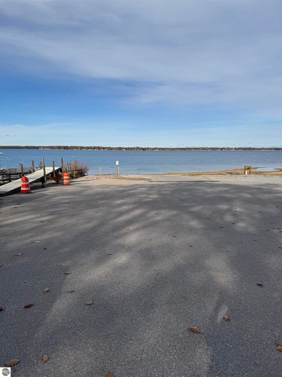 Scenic view of Lake Missaukee with a boat ramp, autumn foliage in the background, and a clear sky, highlighting the outdoor recreational opportunities near the cottage for sale at 1779 S Green Road, Lake City, MI.