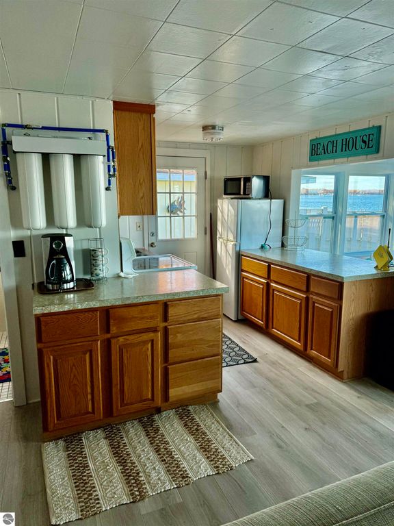Cozy kitchen interior of a cottage on Lake Missaukee, featuring wooden cabinets, a coffee maker, and a sign reading "BEACH HOUSE," with a view of the lake through the window.