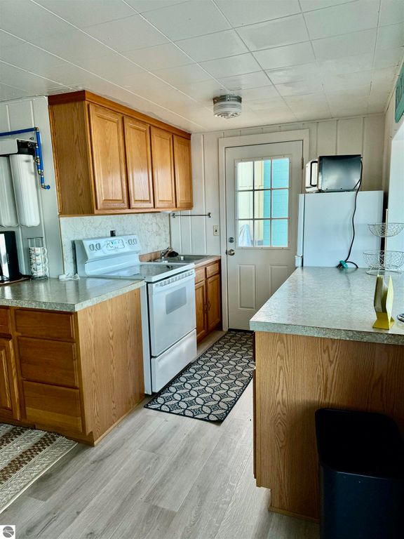 Cottage kitchen interior featuring wooden cabinets, white appliances, and a door leading outside, highlighting the cozy charm of the property at 1779 S Green Road, Lake City, MI.