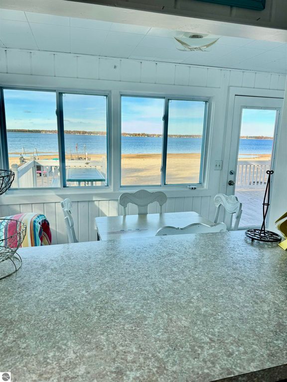 Cottage interior with white walls, dining table, and large windows showcasing Lake Missaukee view, highlighting beach and dock area.