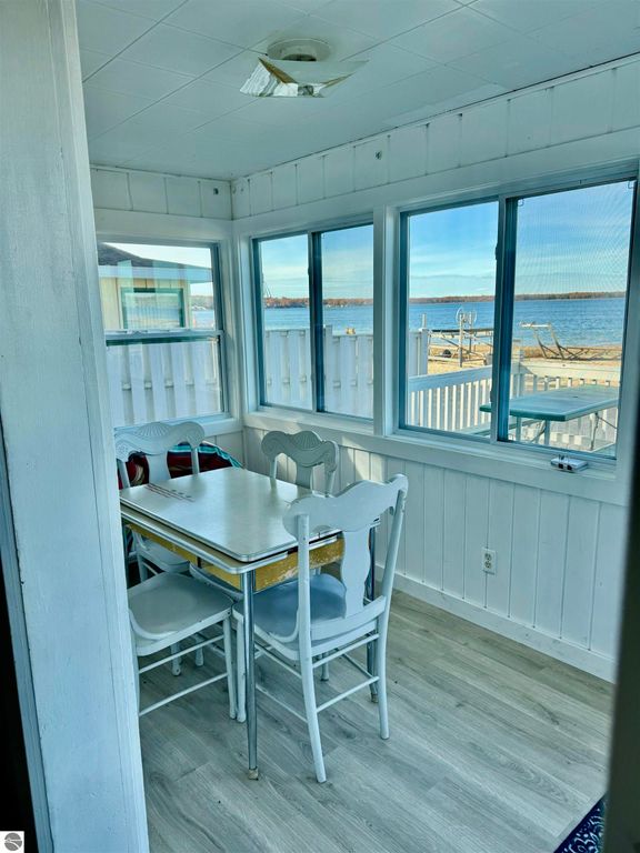Cozy dining area with white chairs and table, windows overlooking Lake Missaukee, bright natural light, part of a charming cottage for sale in Lake City, MI.