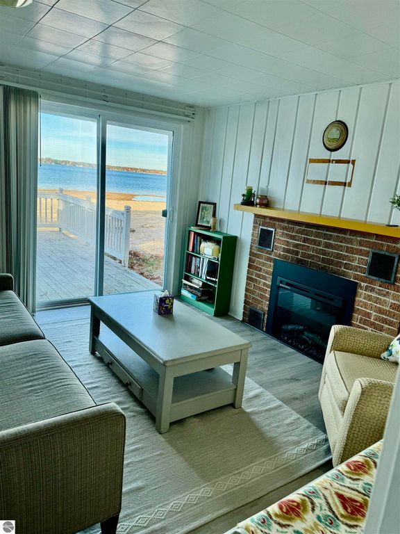 Cozy living room with lake view, featuring a fireplace, coffee table, and sliding glass doors leading to a deck on Lake Missaukee, showcasing the charm of the cottage for sale at 1779 S Green Road, Lake City, MI.
