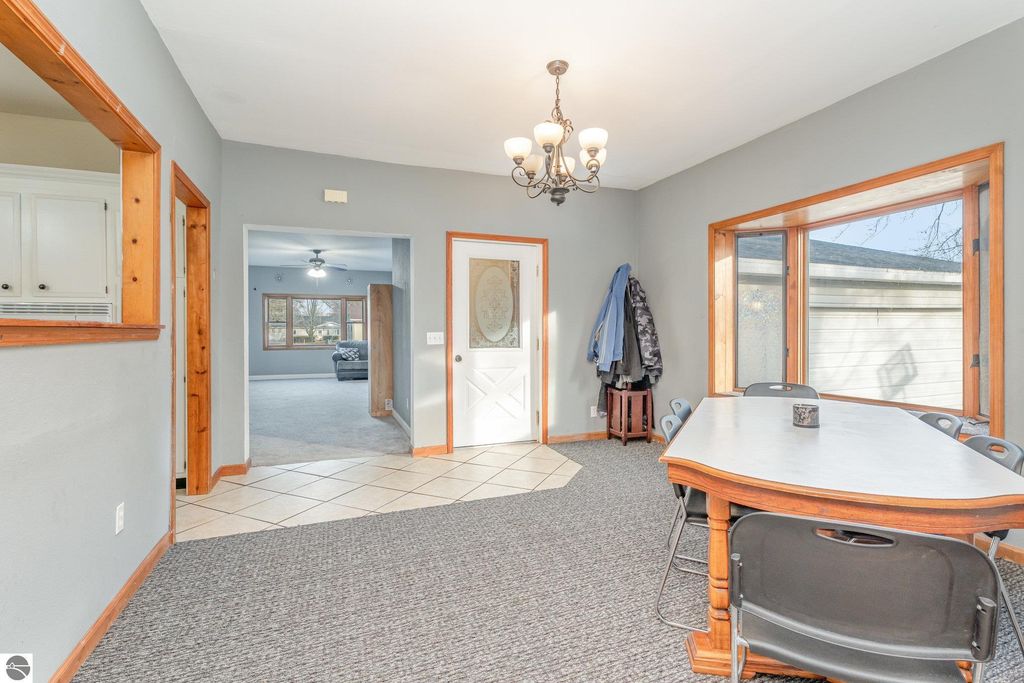 Spacious dining area with chandelier, featuring a table and chairs, connecting to a living room with large windows, in the home located at 1708 W Lyons Street, Mt Pleasant, MI.