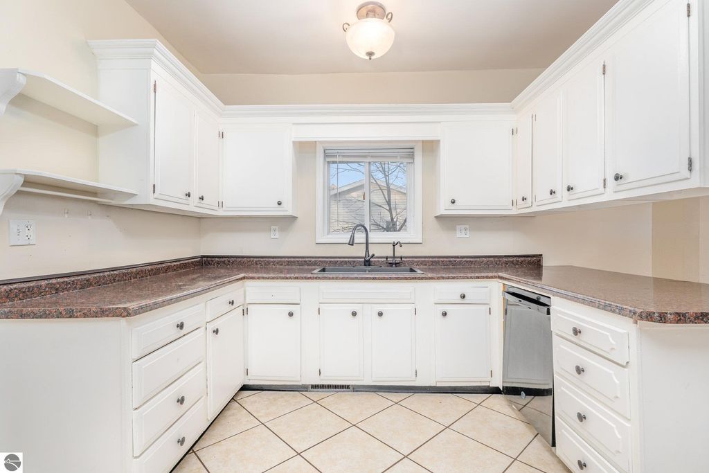 Spacious kitchen with white cabinetry, granite countertops, and stainless steel dishwasher, featuring a window above the sink and tile flooring, located in the home at 1708 W Lyons Street, Mt Pleasant, MI.